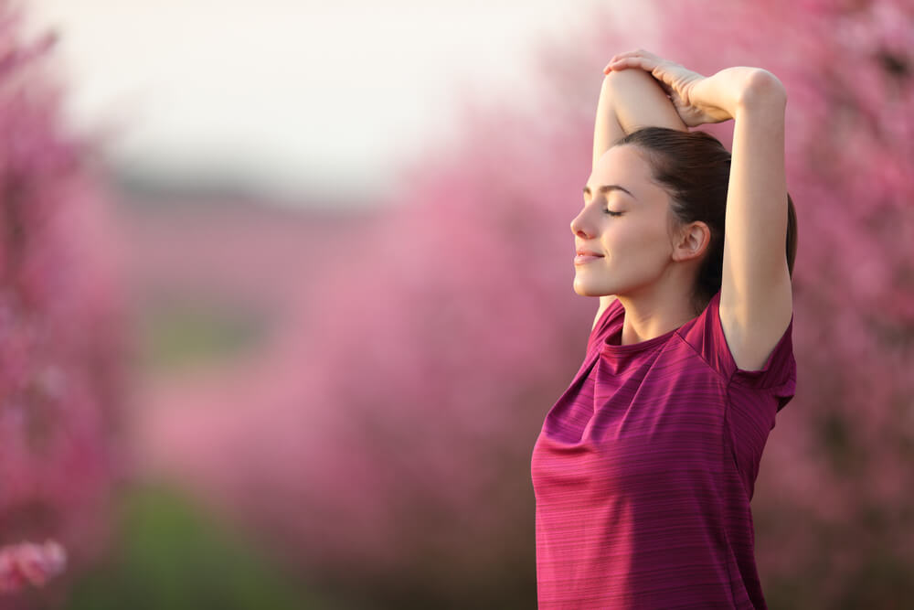 Relaxed runner stretching arms after exercise in a pink flowered field
